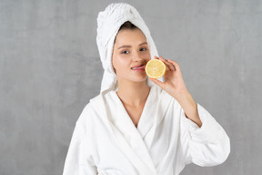 Cheerful woman in bathrobe licking a lemon