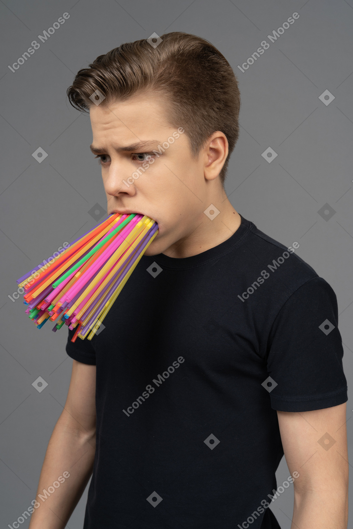 Three-quarter portrait of sad male teenager with plastic straws in mouth