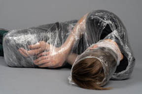 Young man lying down wrapped in plastic