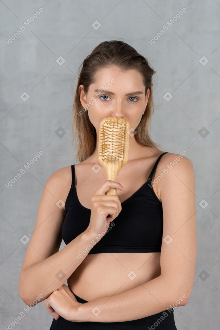 Vista frontal de una mujer joven escondiendo la boca detrás del cepillo para el cabello