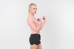 Young blond-haired person in black and pink outfit posing with sports  items against a light grey background
