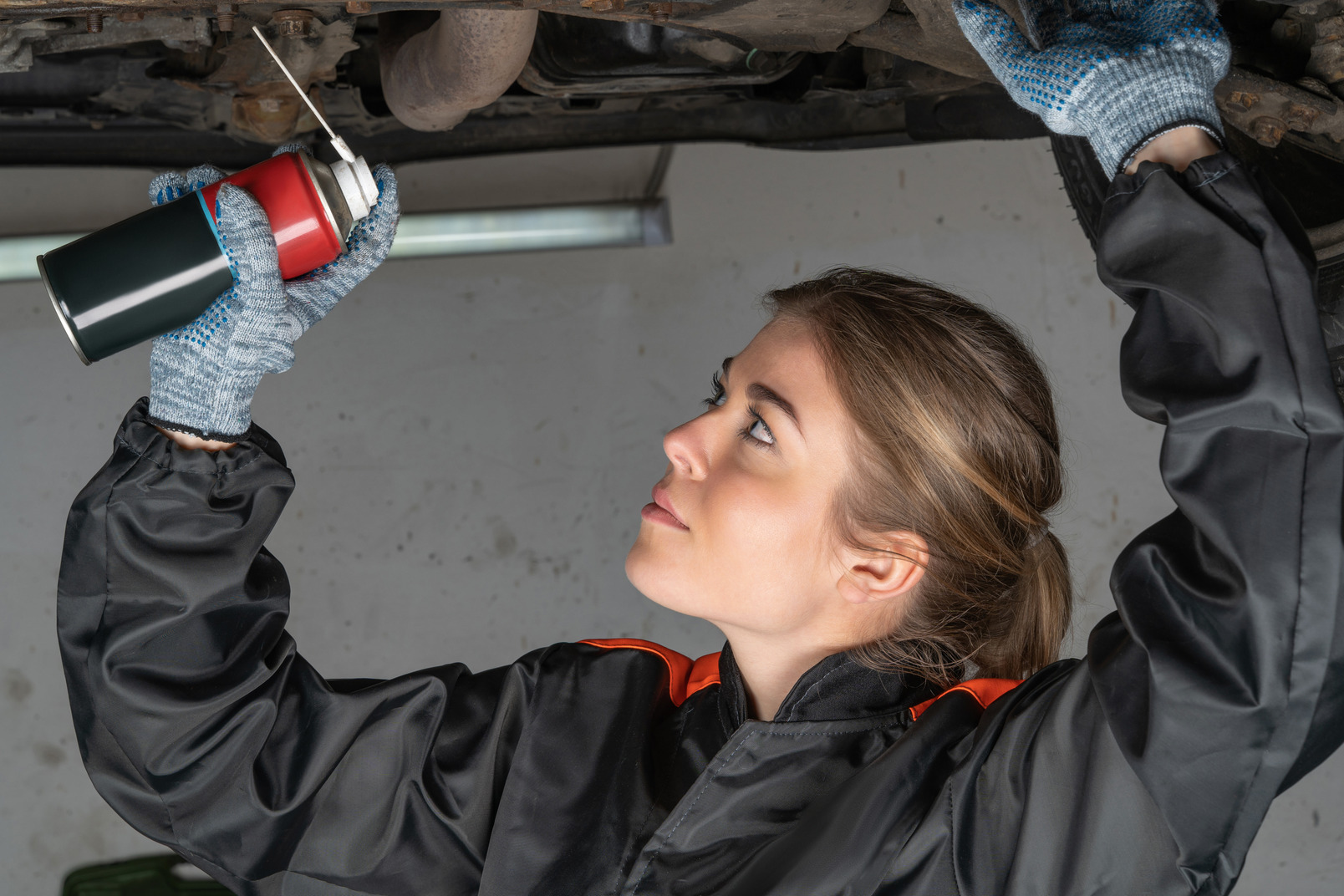 Young woman spraying technical liquid on car mechanisms