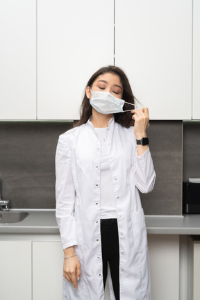 Vista frontal de una doctora tomando máscara con los ojos cerrados