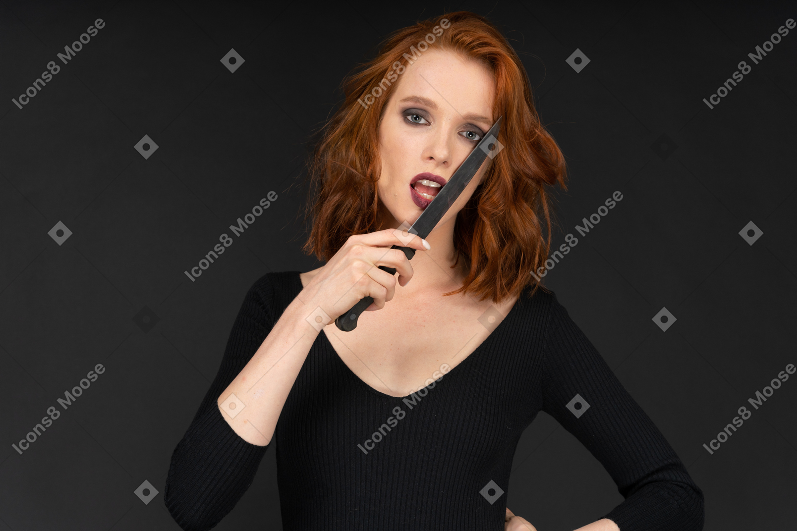 A sexy woman on ther dark background holding the knife close to her mouth