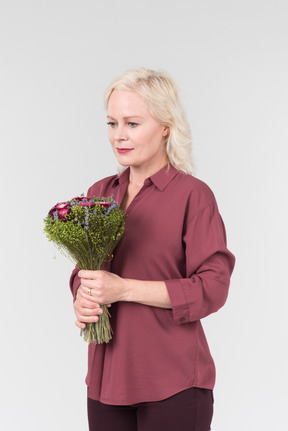 A nice-looking middle-aged blonde woman in a burgundy shirt and with a simple bouquet of flowers in her hands