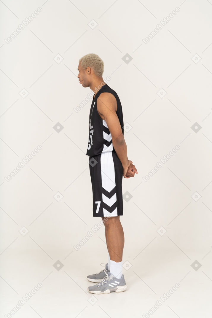 Vista lateral de um jovem jogador de basquete, mordendo os lábios e segurando as mãos atrás