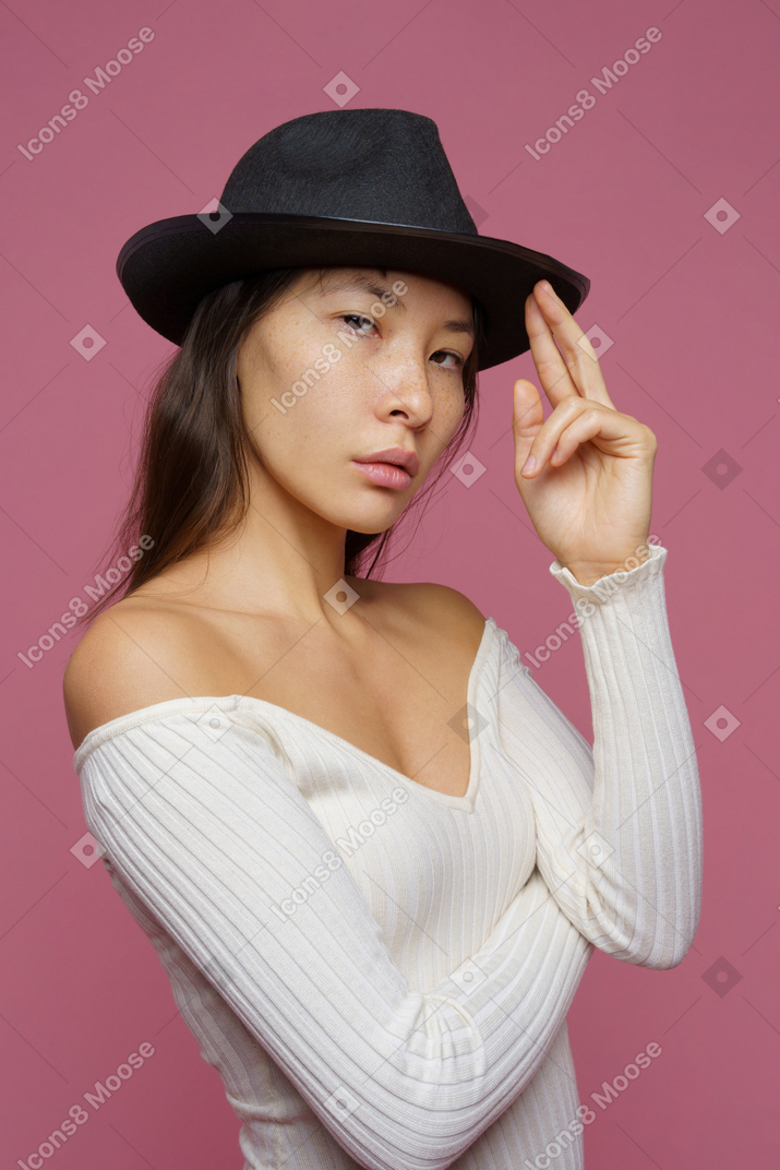 Three-quarter view of a bossy young female touching her black hat