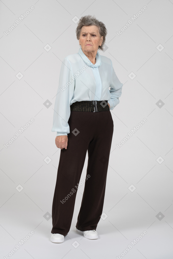 Вид спереди на пожилую женщину, неодобрительно выглядящую с рукой на бедре
