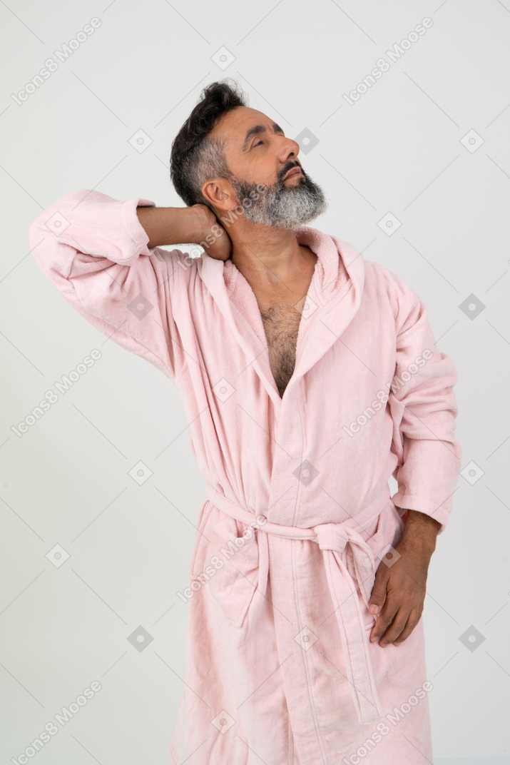 Зрелый мужчина в розовом халате смотрит в сторону и касается шеи