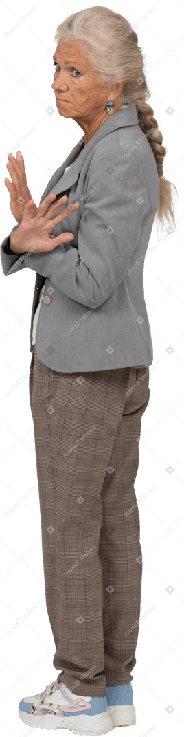 Vista lateral de una anciana en traje mostrando gesto de parada