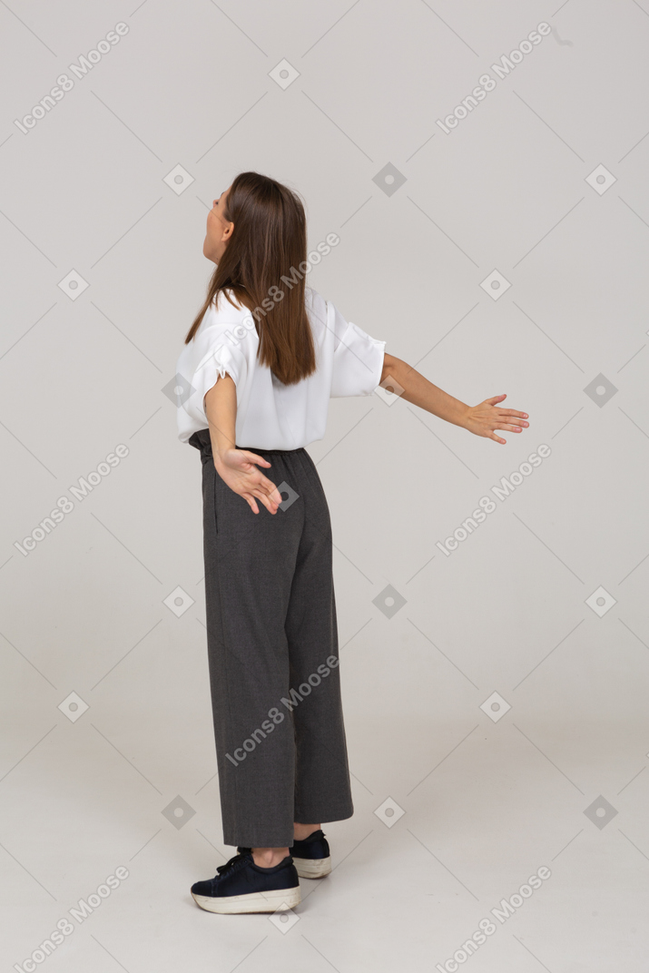 Vista posterior de tres cuartos de una joven en ropa de oficina extendiendo sus brazos