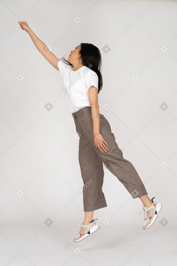 Side view of a jumping young lady in breeches and t-shirt outstretching her hand