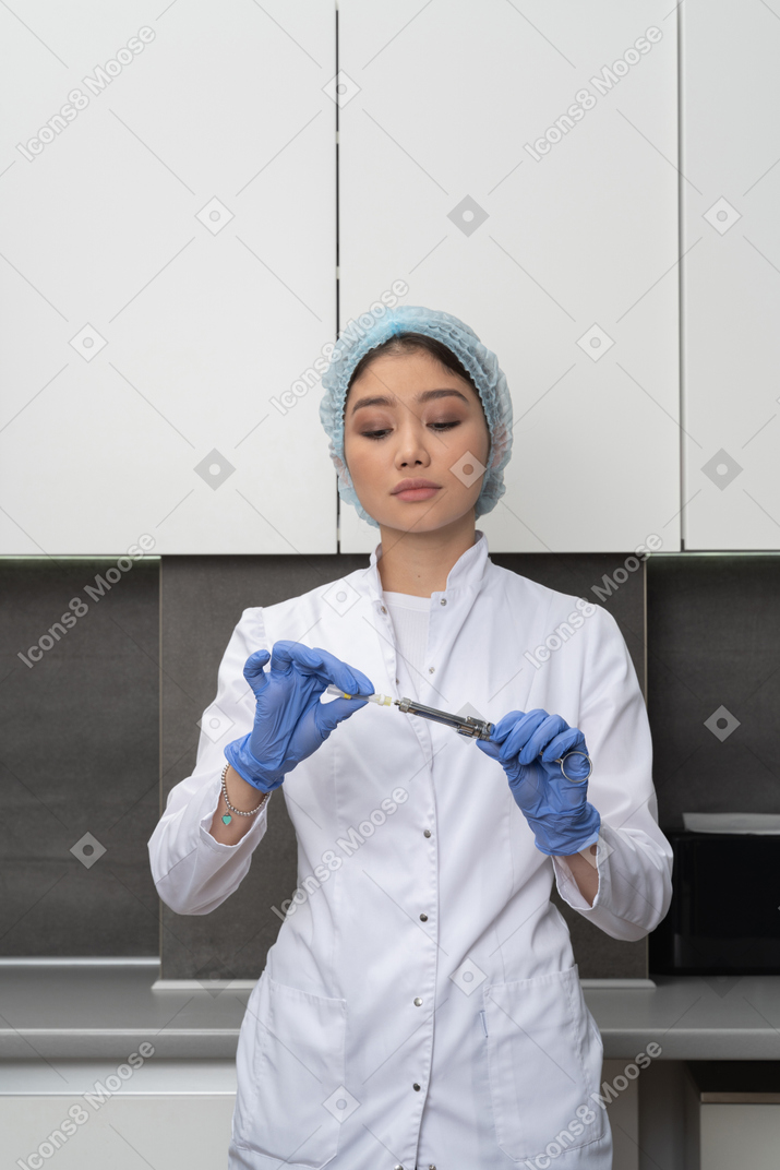 Front view of a female doctor in a medical hat holding a syringe and looking down