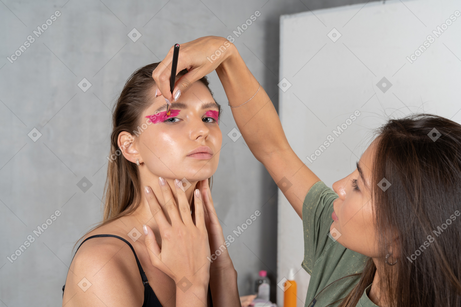 Dreiviertelansicht einer jungen frau mit leuchtend rosa augen make-up & ihrer visagistin