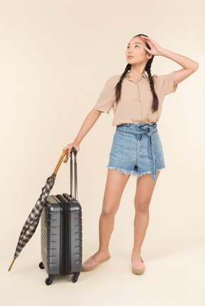 Jeune femme avec valise et parapluie regardant le ciel