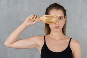 Close-up of a young woman covering one eye with hairbrush