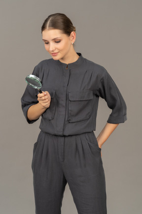 Front view of young woman in a jumpsuit holding a magnifying glass