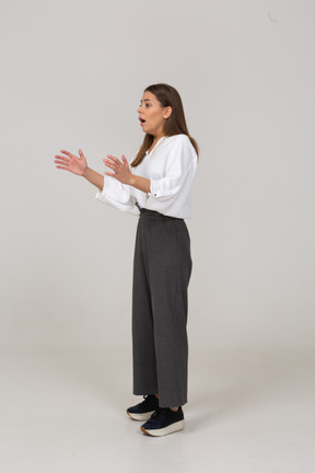 Vista di tre quarti di una giovane donna scioccata in abiti da ufficio che alza la mano