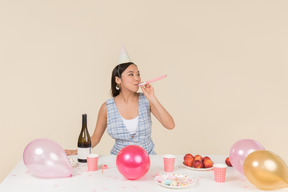 Young asian girl sitting at the birthday table and whistling