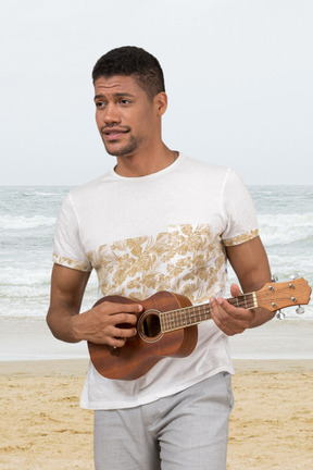A man standing on a beach holding a ukulele