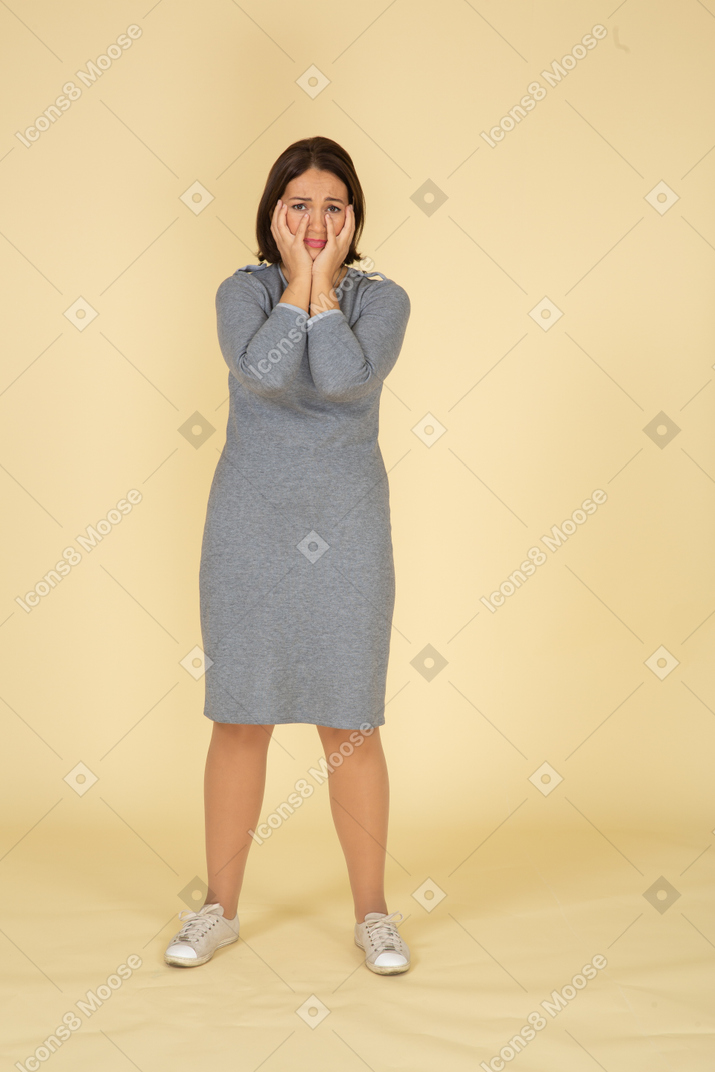 Front view of a sad woman in grey dress touching her face