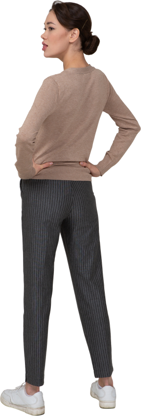 Vista posterior de tres cuartos de una joven en suéter y pantalones poniendo las manos en las caderas