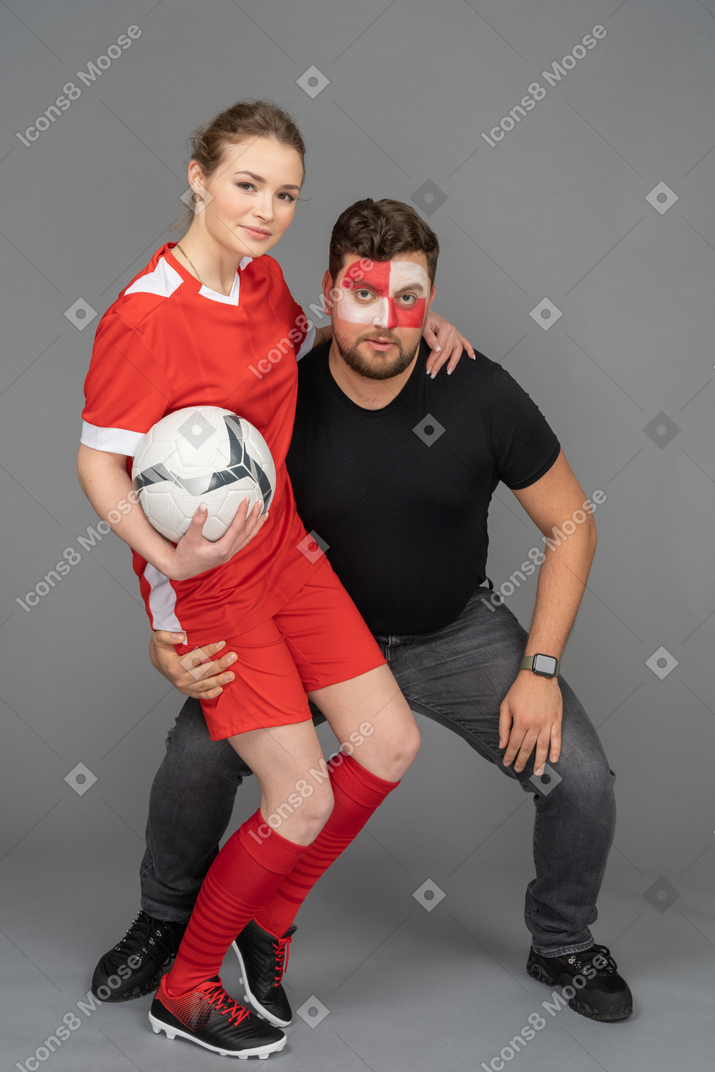 Front view of a male football fan embracing female soccer player