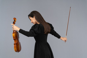 Three-quarter back view of a female violin player in black dress making a bow