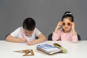 Mädchen, das eine sonnenbrille aufsetzt, und ein junge, der hausaufgaben macht