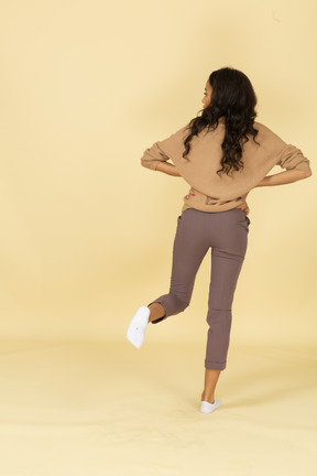 Back view of a dark-skinned young female putting hands on hips while looking aside