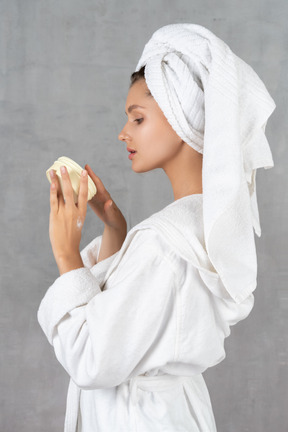 Vista laterale di una donna in accappatoio che applica crema per le mani