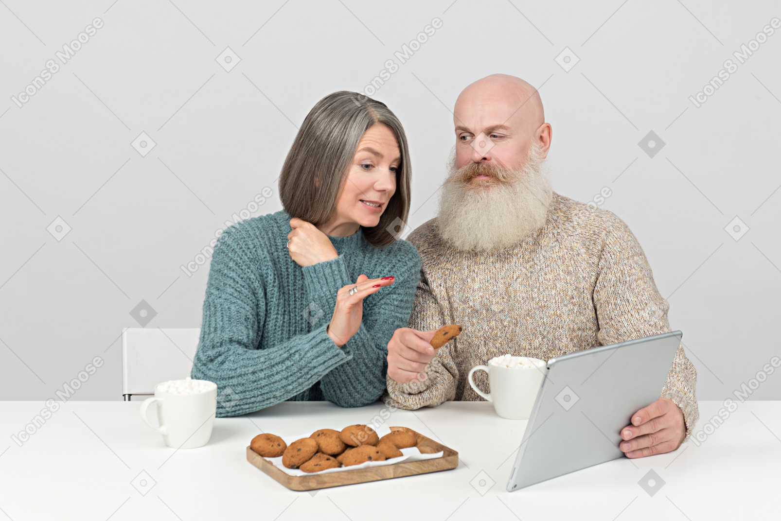 Aged couple sitting at the table and watching movie on tablet