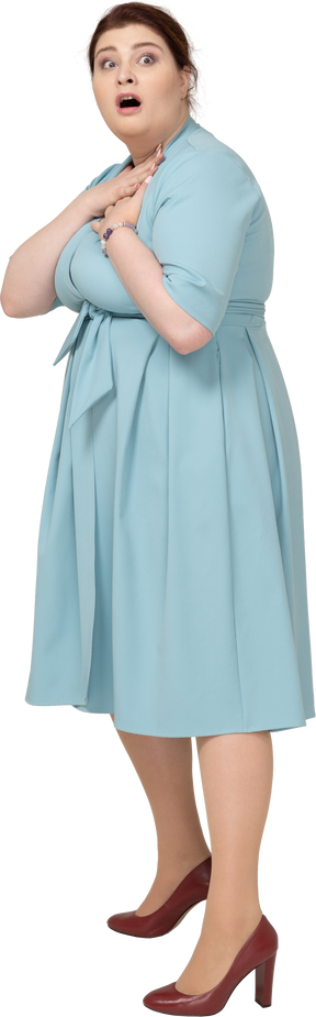 Vista frontal de una mujer sorprendida en vestido azul tocando su cuello
