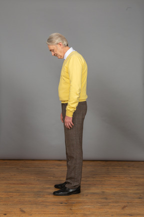 一个黄色的套衫弯下腰，他的眼睛的可悲的老男人的侧视图