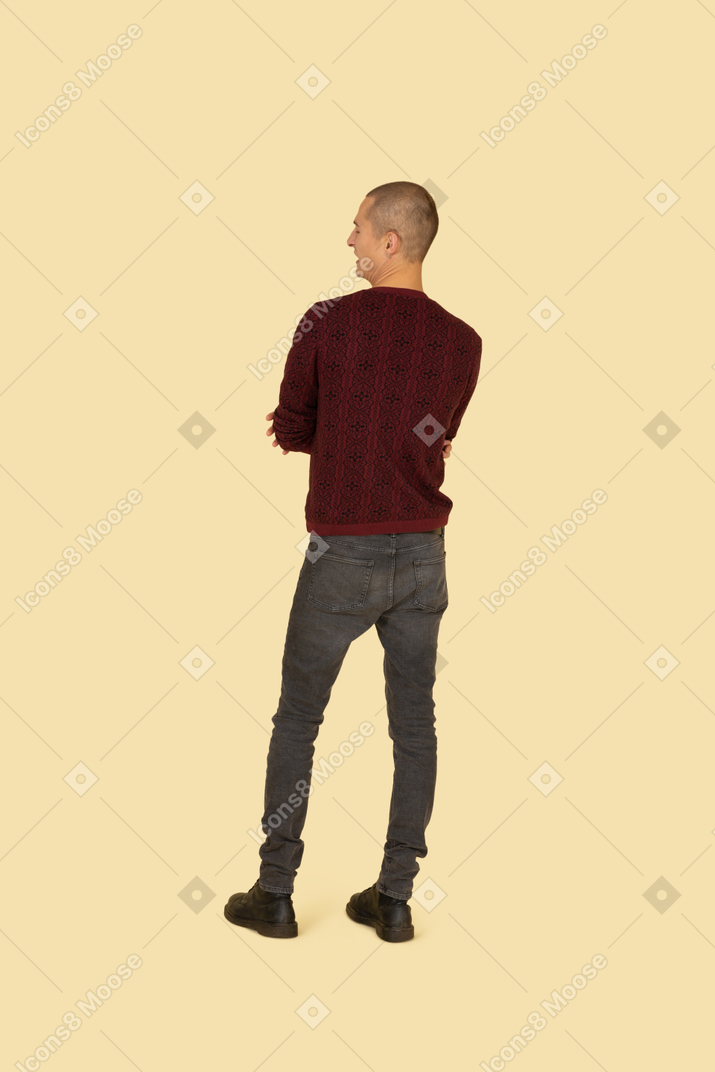 Back view of a displeased young man dressed in casual clothes crossing his hands