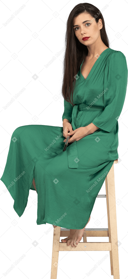 全长的年轻女子，穿着绿色的衣服，坐在椅子上，按住单簧管