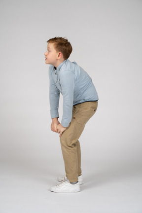 Vista lateral de um menino bonito, inclinando-se e tocando o joelho