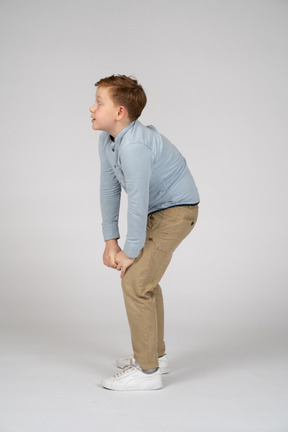 Side view of a cute boy bending down and touching knee