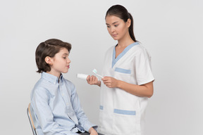 Женский стоматолог, показывая зубную щетку и зубную пасту для малыша мальчика пациента
