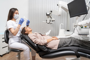 Pleine longueur d'une femme dentiste examinant son patient avec un miroir