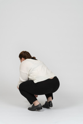 Rear view of a plump woman in casual clothes squatting