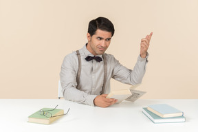 Profesor adulto enojado sentado en la mesa y leyendo un libro