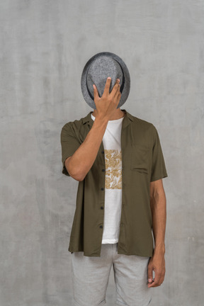 Front view of man in casual clothes covering face with hat
