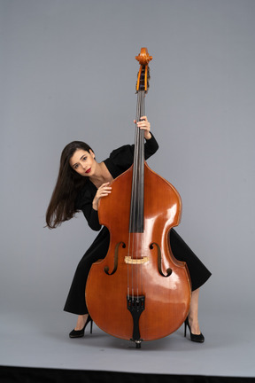 Front view of a young lady squatting behind her double-bass