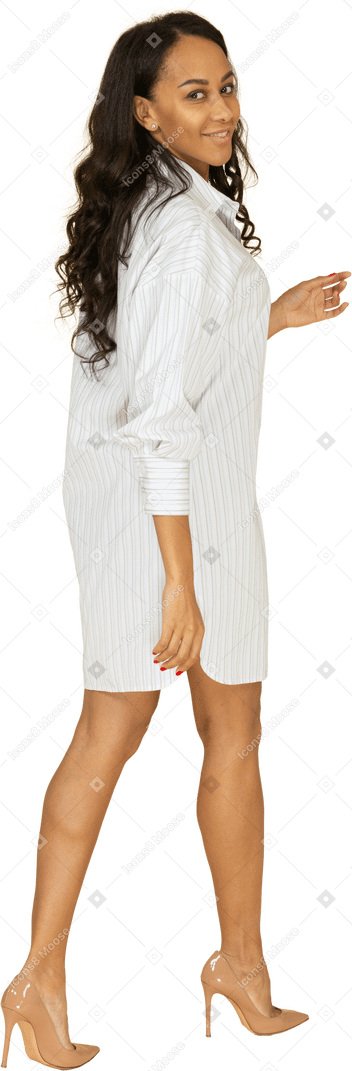 Vista posteriore di tre quarti di una giovane femmina dalla carnagione scura sorridente lasciando in abito bianco