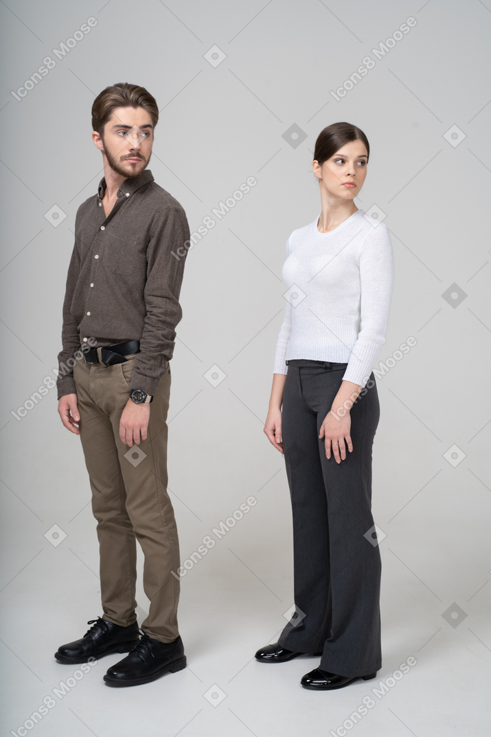 Трехчетвертный вид молодой пары в офисной одежде, поворачивающей голову