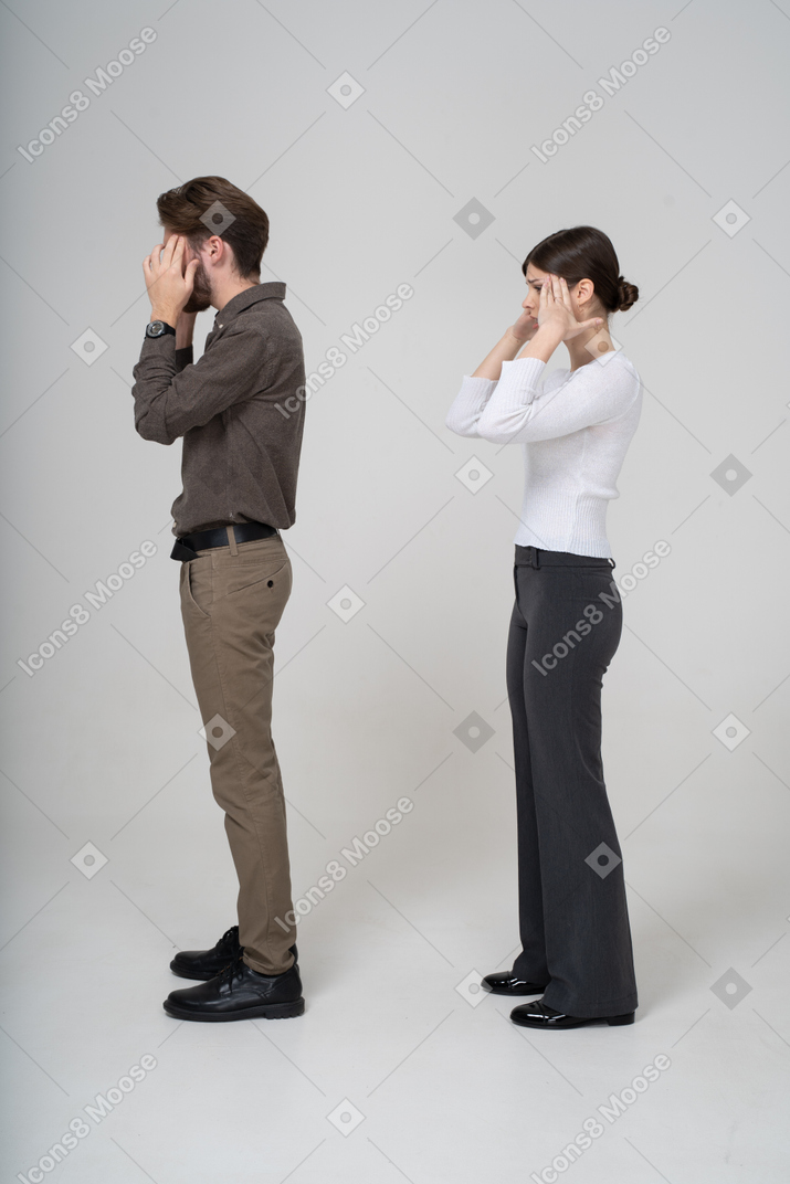 Vista lateral de una pareja joven conmocionada en ropa de oficina tocando la cabeza
