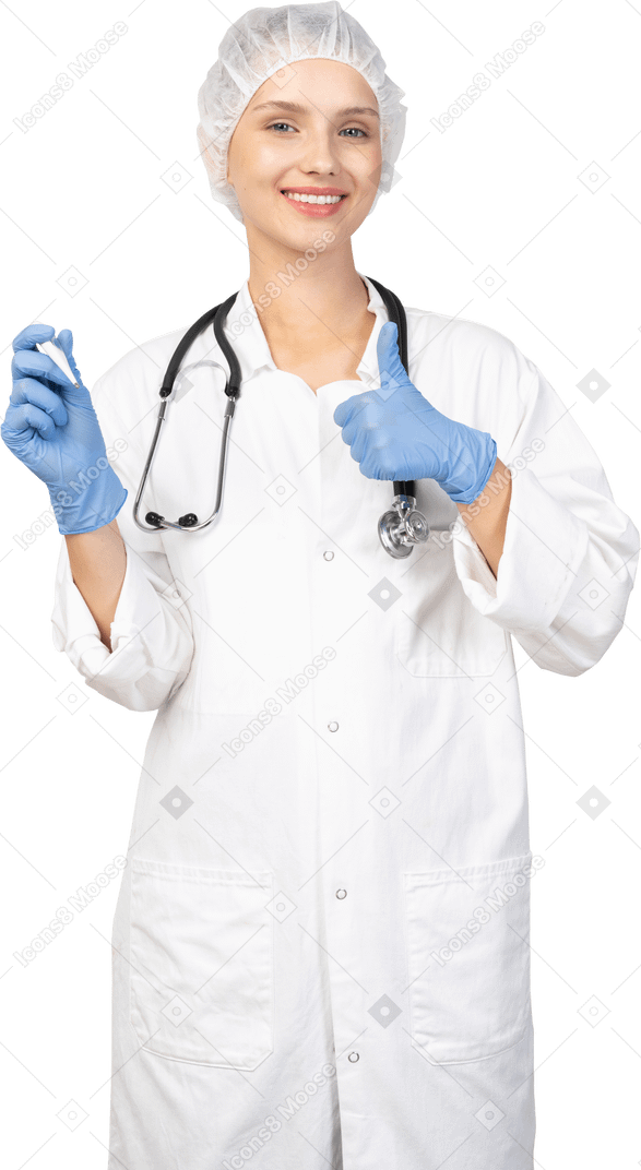 Vista frontal de uma jovem médica sorridente com estetoscópio segurando o termômetro e mostrando o polegar