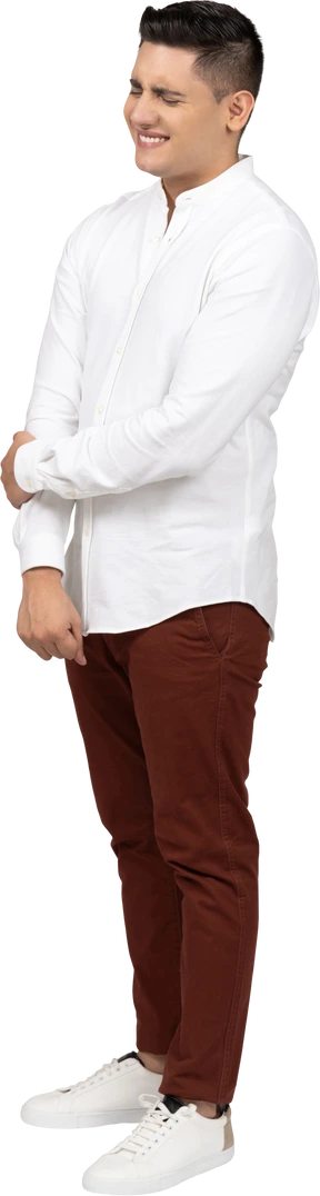 Three-quarter view of a young latino man holding his hand and smiling painfully