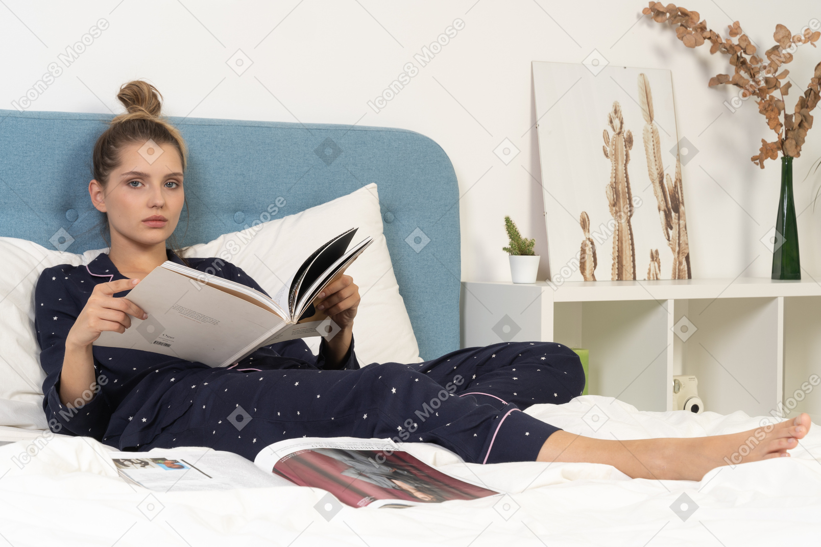 Full-length of a young female in pajama laying in bed while reading fashion magazine